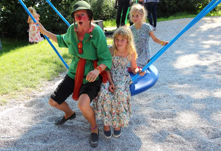 Abbildung: Daily tous les jours, »Musical Swings«, Clownin Murmel und zwei Kinder weihen die Schaukeln ein